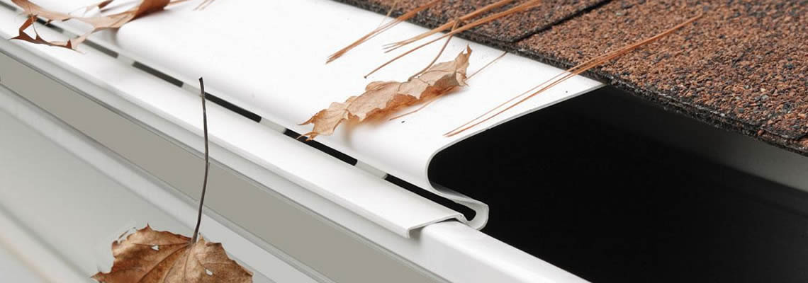 A white gutter guard is installed on the roof and several leaves fall on it.